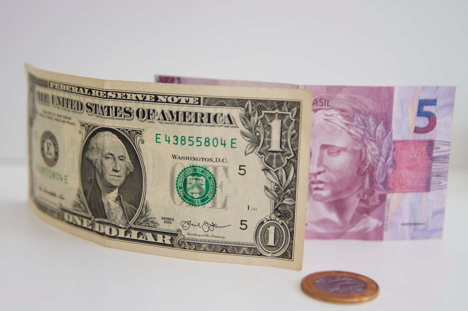Cédula de US$ 1 ao lado de cédula de R$ 5 e moeda de 1 real