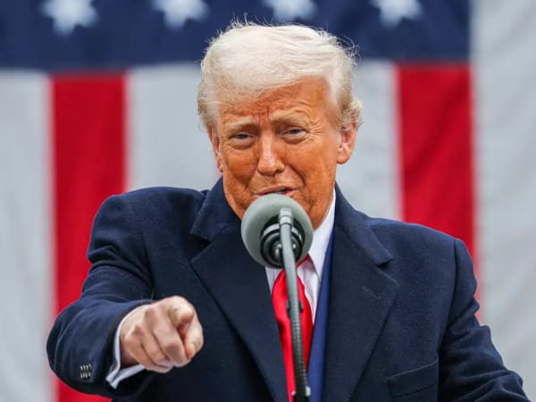 Donald Trump aponta o dedo ao falar ao microfone diante de uma bandeira dos Estados Unidos