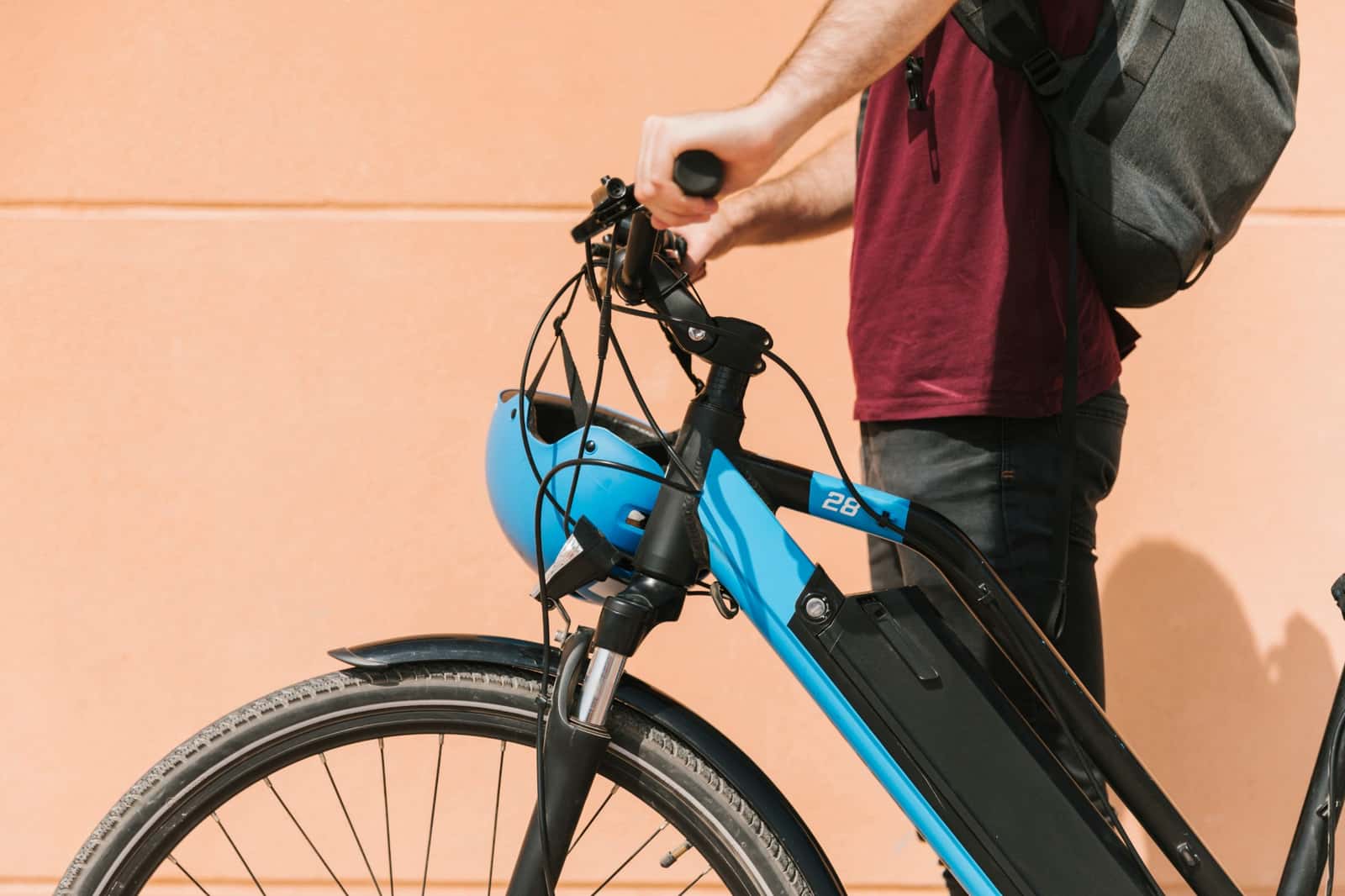 Pessoa segurando o guidão de uma bicicleta elétrica, com capacete azul pendurado no volante