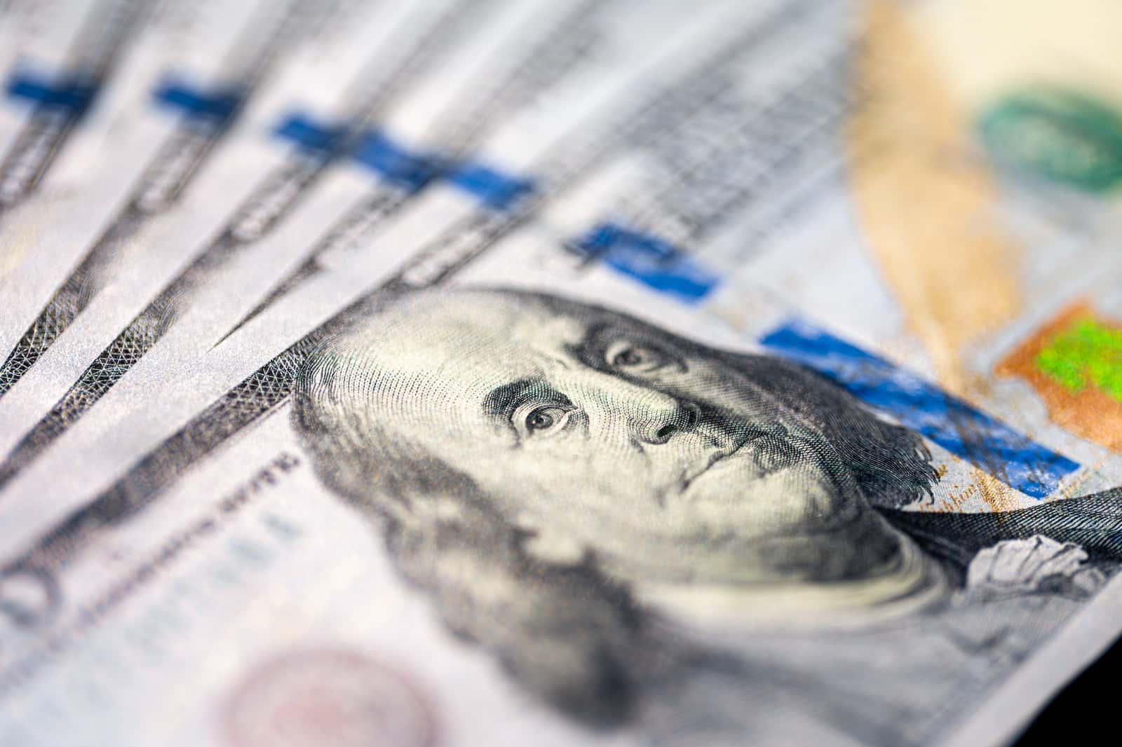 Notas de cem dólares americanos em close, dispostas em leque