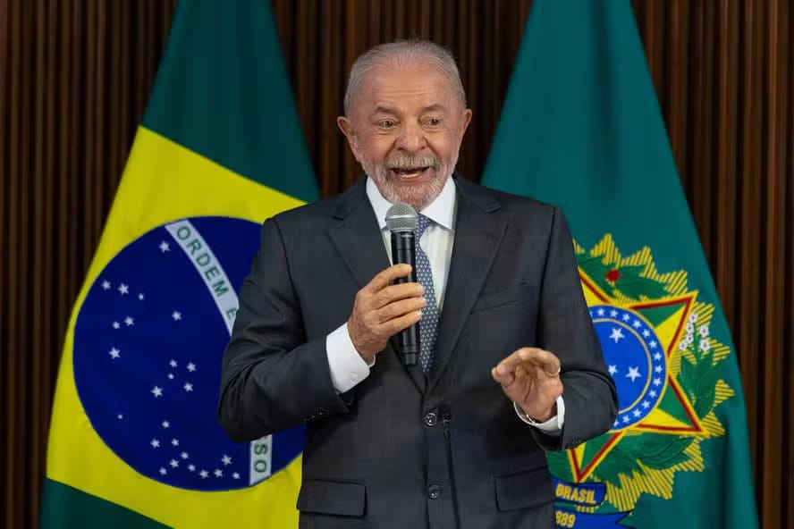 O presidente Lula fala ao microfone diante da bandeira do Brasil e do brasão da República