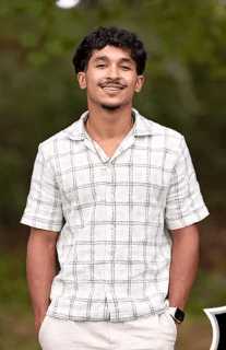 Jovem brasileiro sorri em foto ao ar livre, com camisa xadrez de manga curta