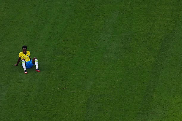 Vinicius Junior sentado sozinho no gramado, abatido, após a eliminação do Brasil para a Noruega nas oitavas de final da Copa do Mundo 2026