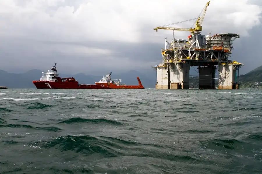 Plataforma de petróleo offshore com dois navios de apoio em mar aberto, sob céu nublado