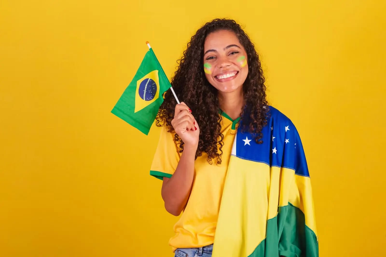 Mulher sorridente segurando uma bandeira do Brasil, com o rosto pintado de verde e amarelo
