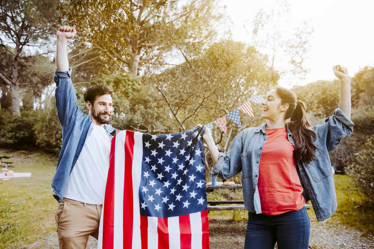 Casal comemorando ao ar livre segurando uma bandeira dos Estados Unidos em uma confraternização