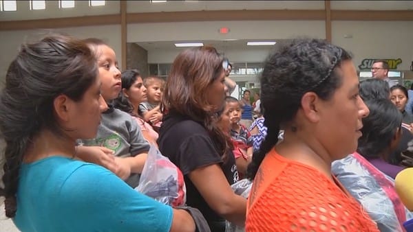 Famílias com crianças de colo aguardam em pé em um salão durante atendimento