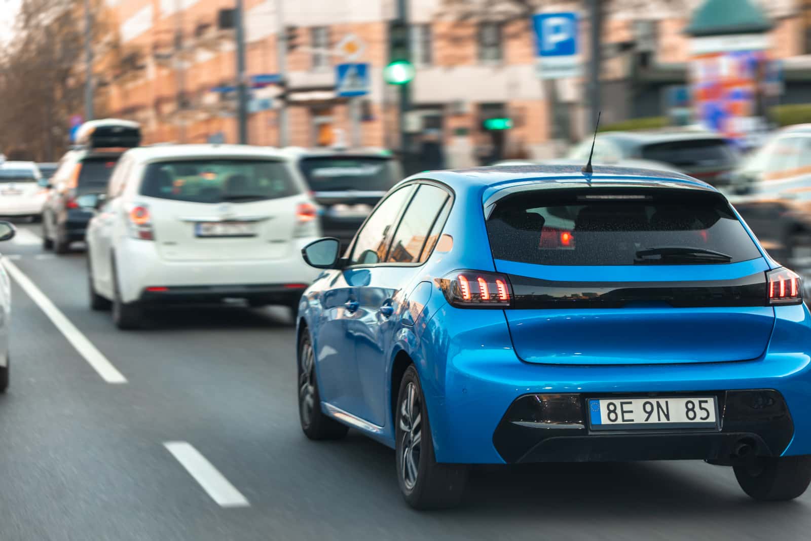 Traseira de um carro azul no trânsito de uma avenida, com a placa à vista