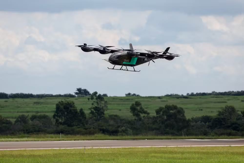 Aeronave elétrica de decolagem vertical da Eve, com múltiplas hélices, paira sobre uma pista de pouso com campo verde ao fundo