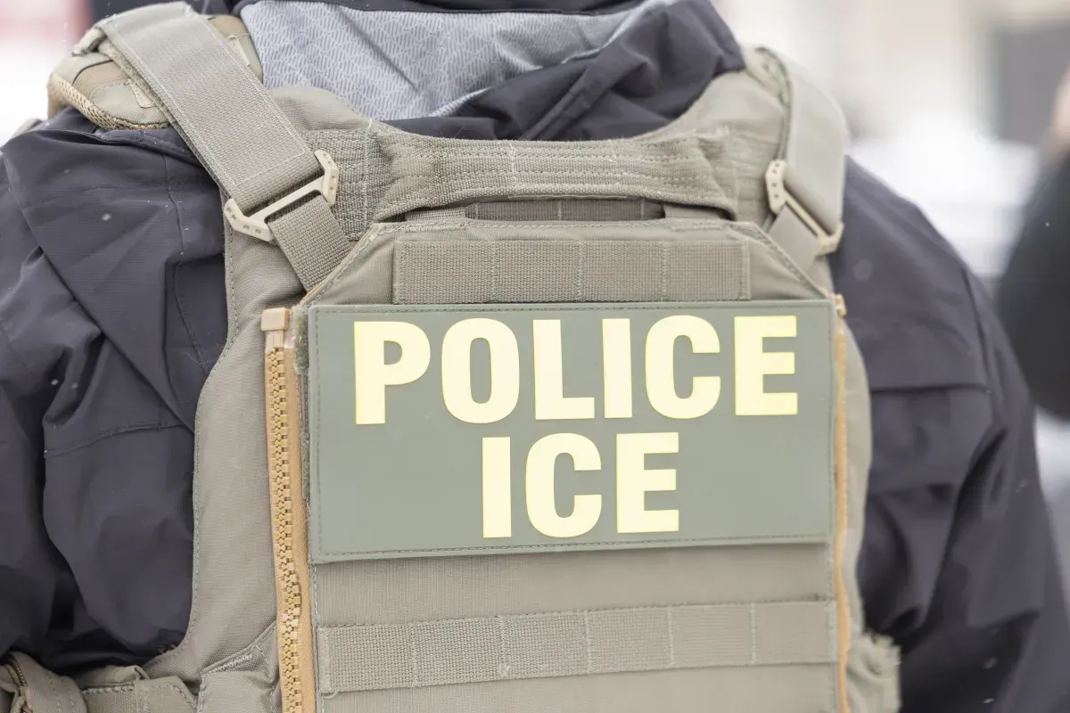 Close das costas de um colete tático com a inscrição POLICE ICE em letras claras