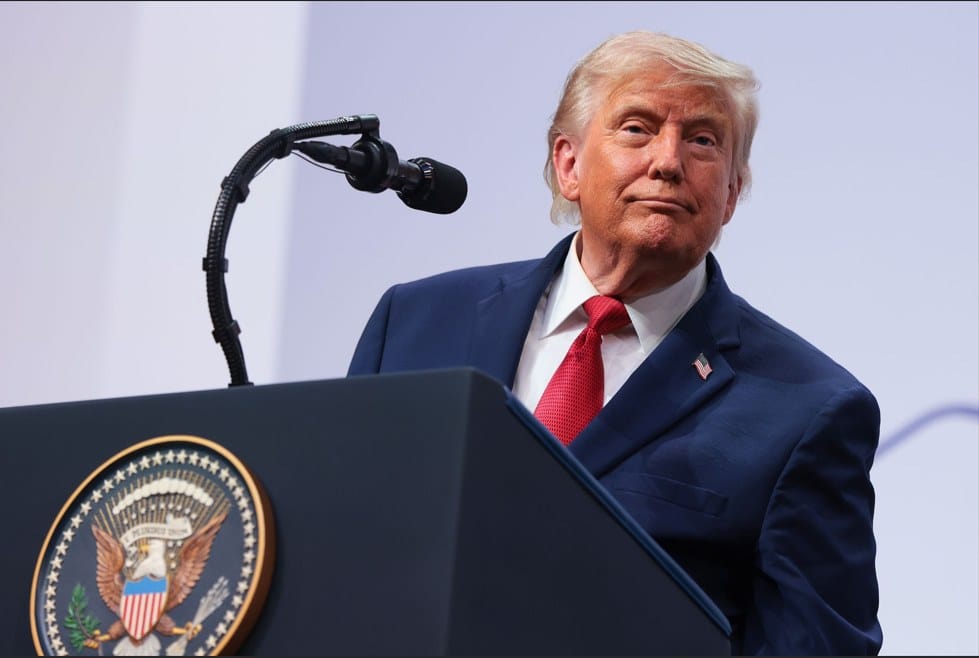 Donald Trump, de terno azul e gravata vermelha, atrás de um púlpito com o selo presidencial dos Estados Unidos, olhando para o lado