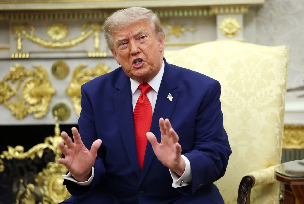 Donald Trump, de terno azul e gravata vermelha, gesticula com as duas mãos enquanto fala sentado no Salão Oval da Casa Branca