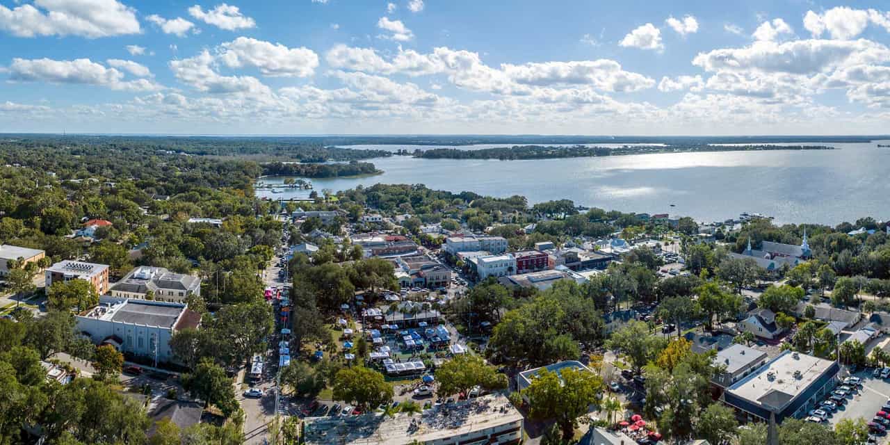 Vista aérea de uma cidade da Flórida Central às margens de um grande lago, com casas, comércio e vegetação sob céu azul com nuvens