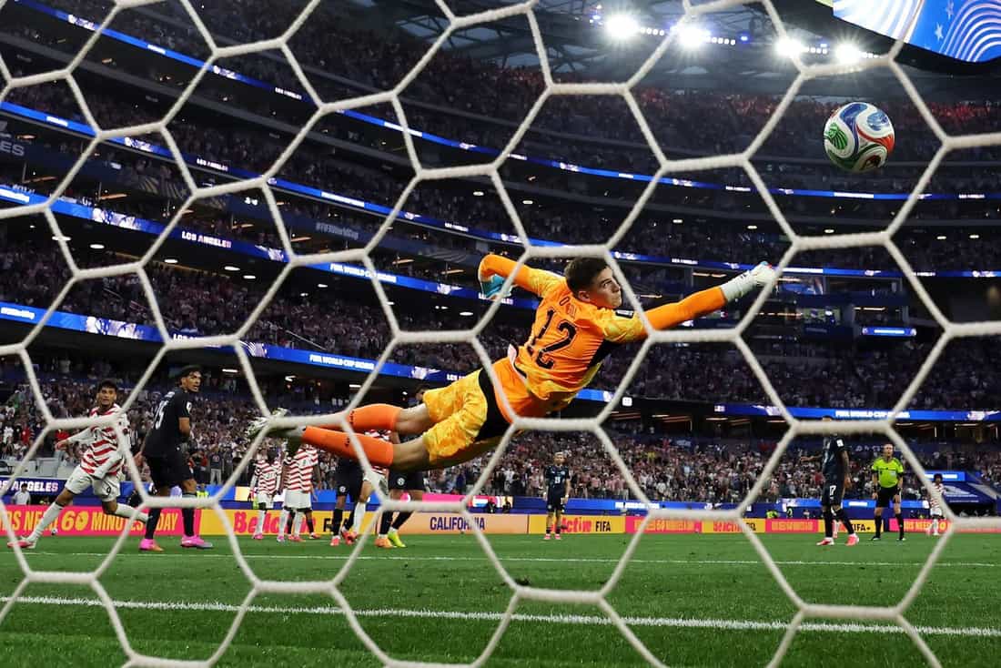 Goleiro se estica no ar para tentar defender a bola em jogo da Copa do Mundo de 2026, em estádio lotado nos Estados Unidos