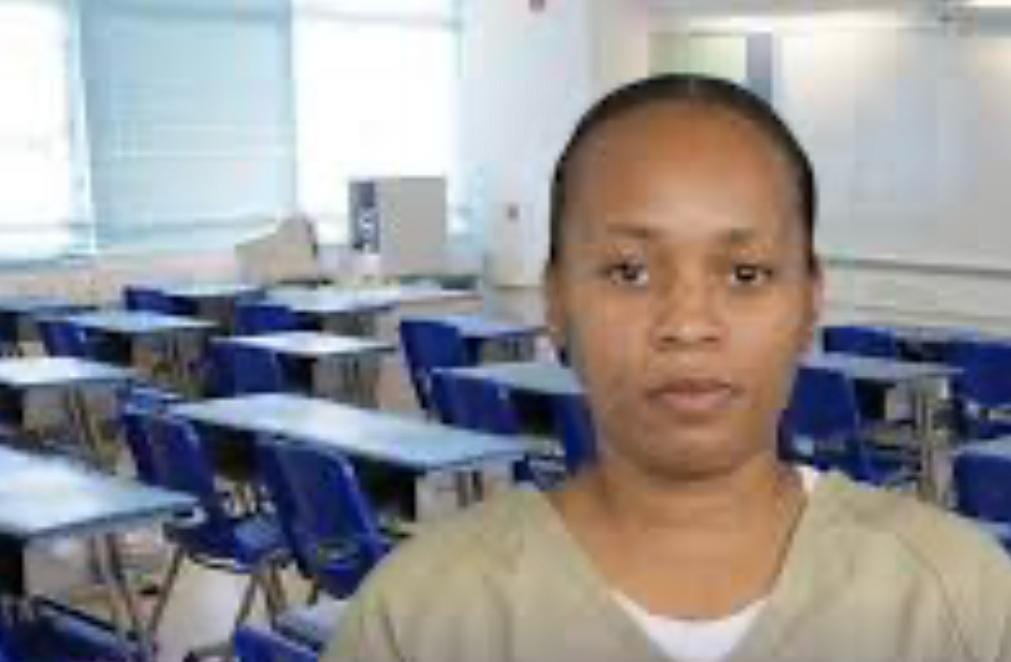 Mulher de uniforme observa a câmera em ambiente que lembra uma sala de provas